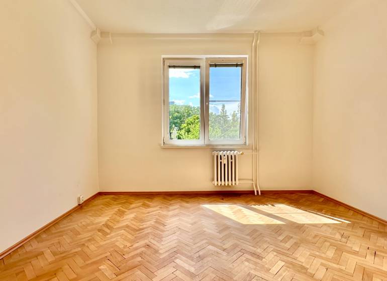 Ein leerer Raum in einer 3-Zimmer-Wohnung mit Parkettboden und einem Fenster mit Blick ins Grüne.