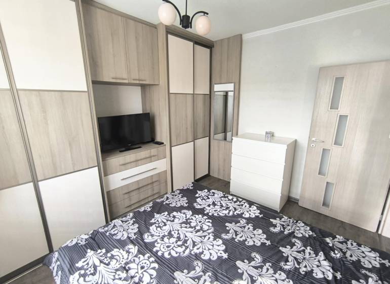 Schlafzimmer in einer 2-Zimmer-Wohnung mit Bett, Schrank, Fernseher und Einbauschrank.