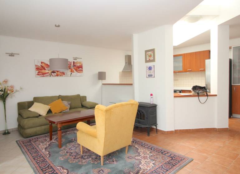 Wohnzimmer mit Teppich, grünem Sofa, gelbem Sessel und Küchenzeile in einem Einfamilienhaus.