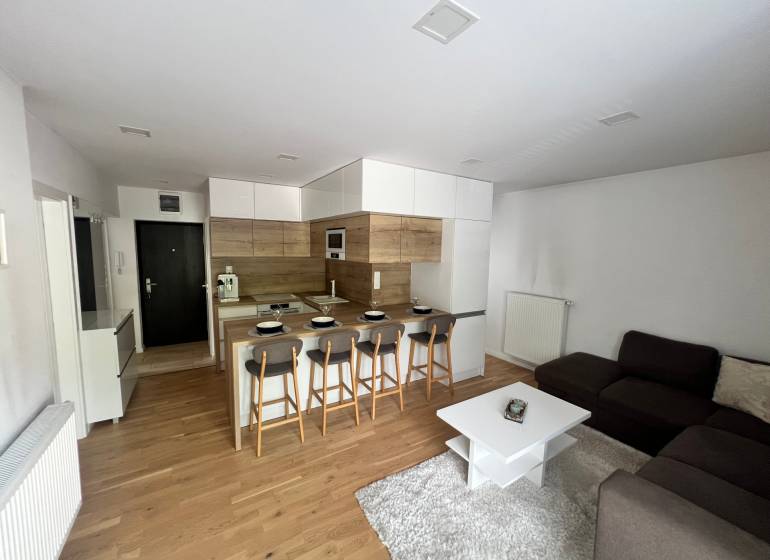 Wohnbereich einer 3-Zimmer-Wohnung mit offener Küche, Bartresen und grauem Sofa.