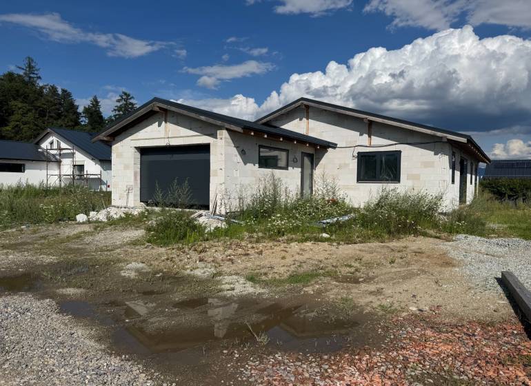 Unvollendetes Einfamilienhaus in Valča mit Garage, umgeben von Natur und Baumaterialien.