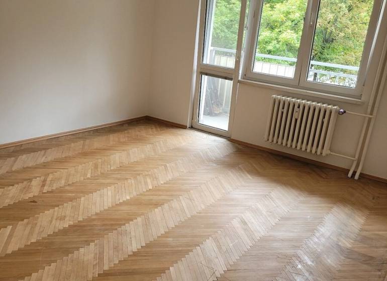 Ein Zimmer in einer 3-Zimmer-Wohnung mit Holzboden und Balkontüren.