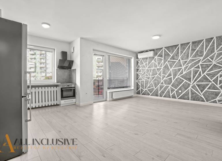 Küche und Wohnzimmer in einer Zweizimmerwohnung mit Holzboden und geometrischer Wand.