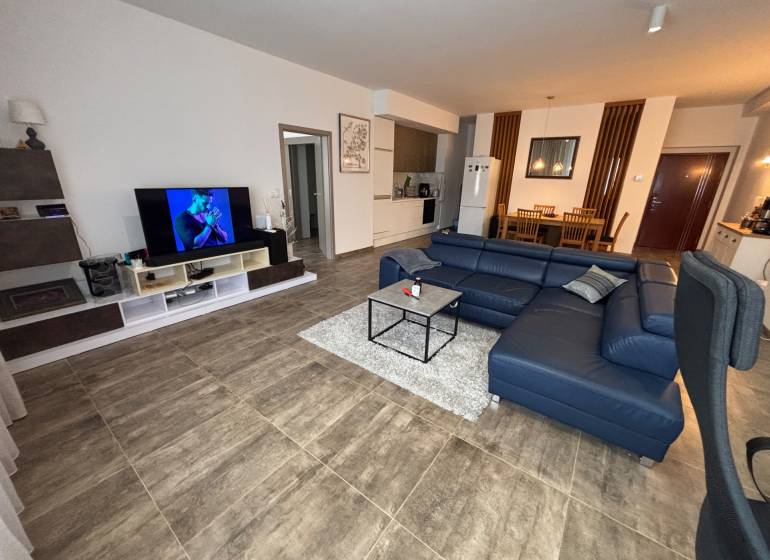 Wohnzimmer in einer Zweizimmerwohnung mit dunklem Sofa und Fernseher, Boden mit Holzdekor.