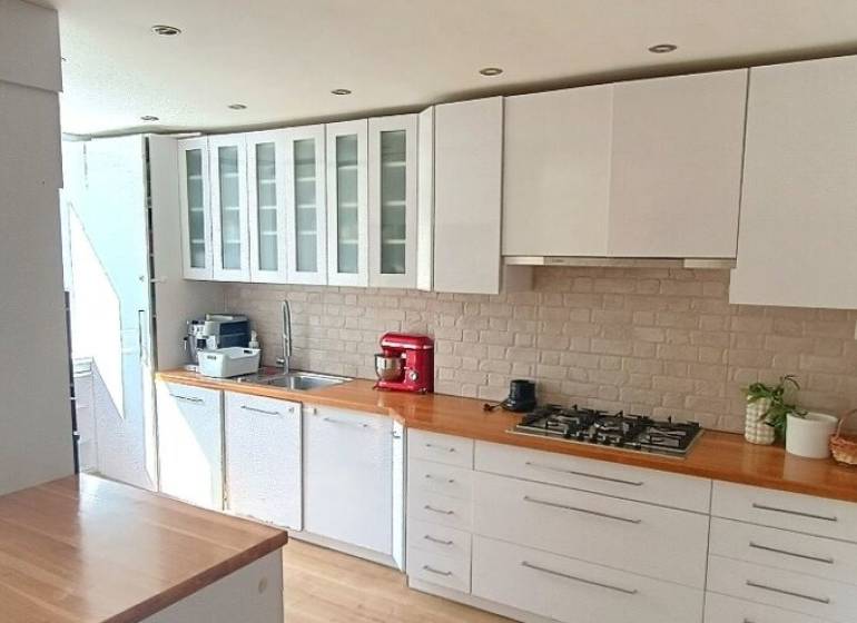 Küche in einer 3-Zimmer-Wohnung mit weißen Möbeln und Herd, Boden mit Holzdekor.