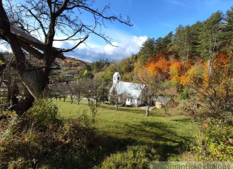 Herbst in den Gärten von Hlboké nad Váhom mit einer kleinen Kirche zwischen den Bäumen, bunte Wälder im Hintergrund.