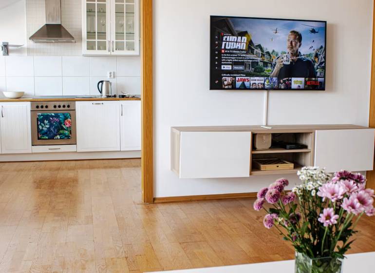 Küche in einer 3-Zimmer-Wohnung mit einem Fernseher an der Wand und Blumen auf dem Tisch.
