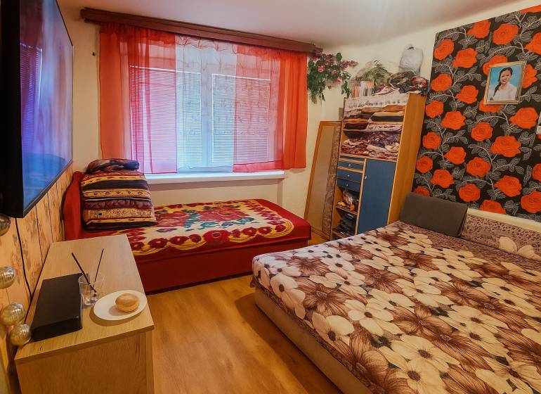 Schlafzimmer in einer 2-Zimmer-Wohnung mit Holzboden und bunten Bettbezügen.