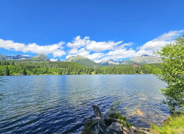 Der See in Štrba, umgeben von landwirtschaftlichen und forstwirtschaftlichen Flächen, mit Gebirgen und blauem Himmel.