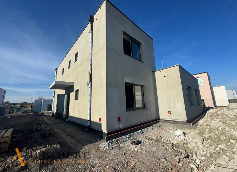 Ein im Bau befindliches Einfamilienhaus in Hubice mit minimalistischem Äußeren und benachbarten Gebäuden.