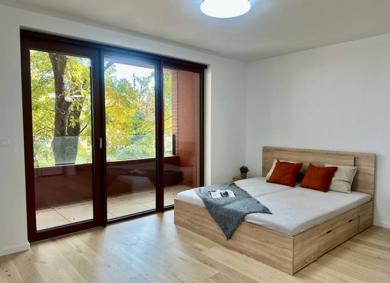 1-Zimmer-Wohnung mit großen Fenstern, Holzboden, Balkon und Bett.