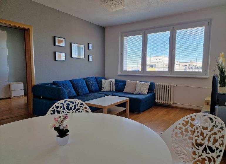 Wohnzimmer einer 3-Zimmer-Wohnung mit Sofa, weißem Tisch und Boden in Holzoptik.