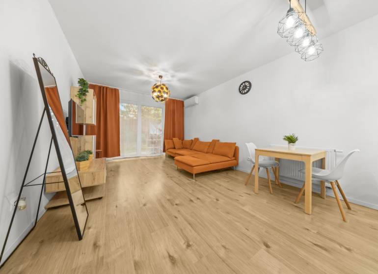 Wohnzimmer in einer Zweizimmerwohnung mit Holzboden, orangefarbenem Sofa und Esstisch.