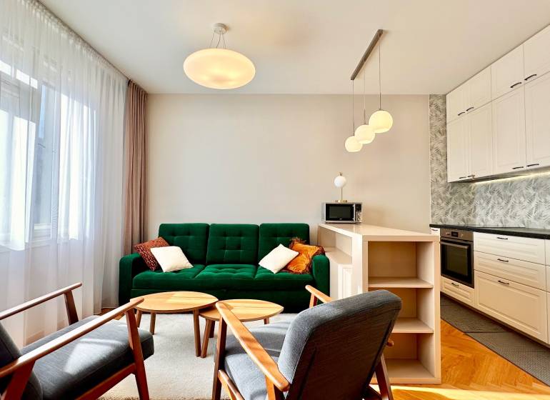 Helles Wohnzimmer mit Küche, grünes Sofa, Holzelemente, drei Lampen.