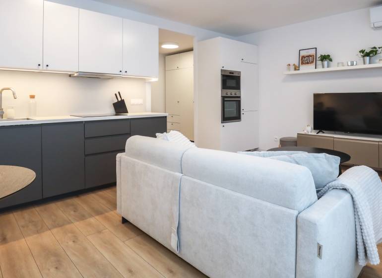 Wohnzimmer einer Einzimmerwohnung mit Küchenzeile, Sofa und Boden in Holzoptik.