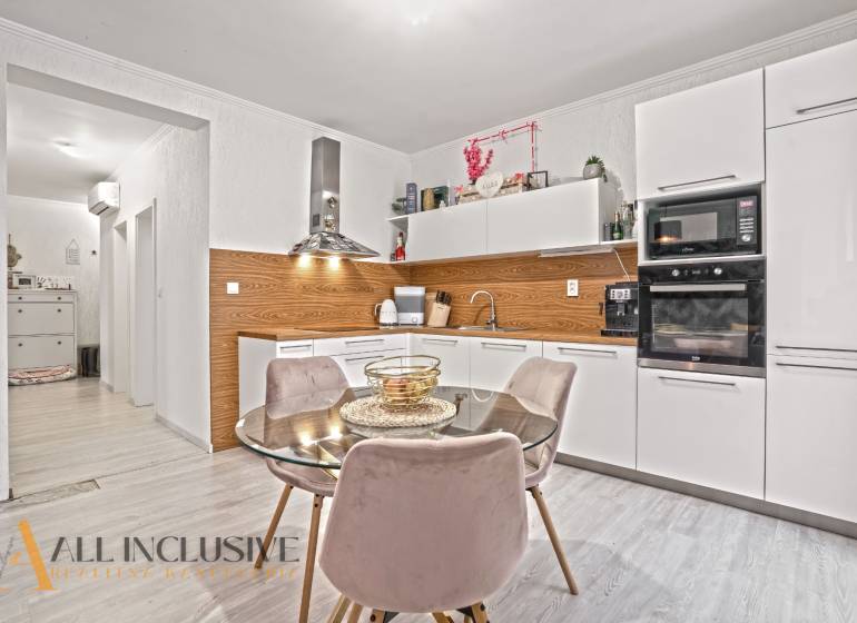 Küche in einer 3-Zimmer-Wohnung mit weißen Schränken, Boden in Holzoptik und Esstisch.