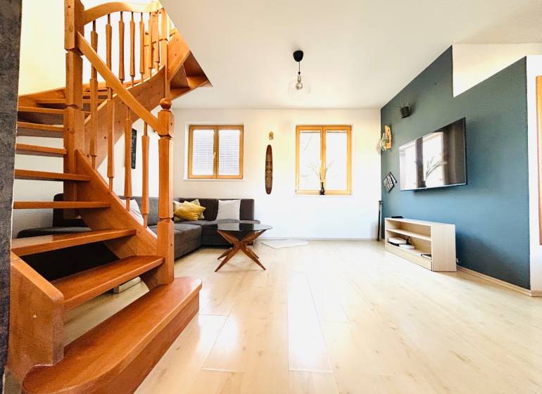 Wohnzimmer mit Holztreppe, Holzboden und Fernseher in einer Zweizimmerwohnung.