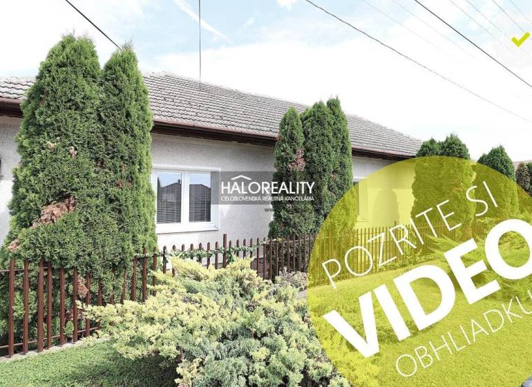 Ein Einfamilienhaus in Veľký Kýr mit einem gepflegten Garten, grünen Thujen und einem Zaun.