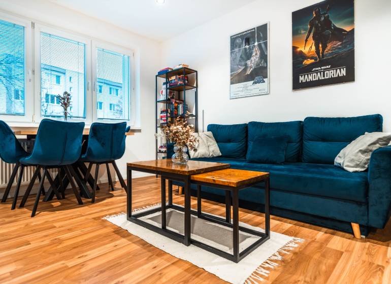 Wohnzimmer in einer 2-Zimmer-Wohnung mit einem blauen Sofa und einem Boden in Holzoptik.