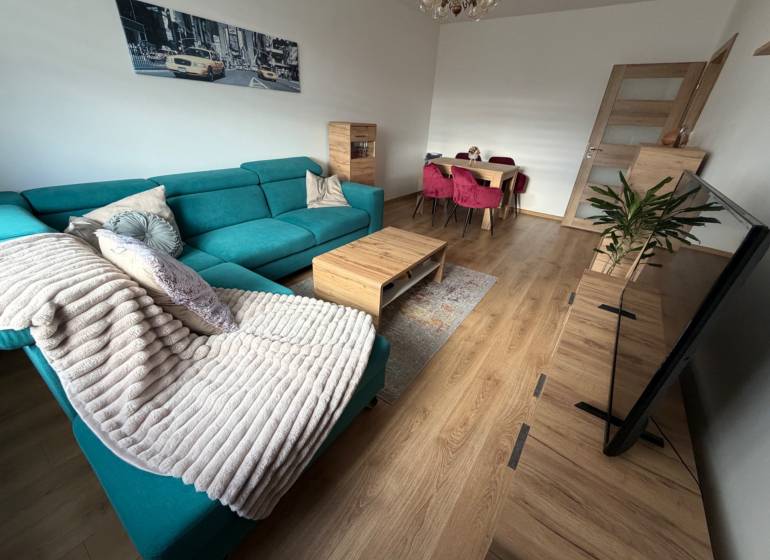 Wohnzimmer einer 4-Zimmer-Wohnung mit einer türkisfarbenen Couch, einem Boden in Holzoptik und einem Esstisch.