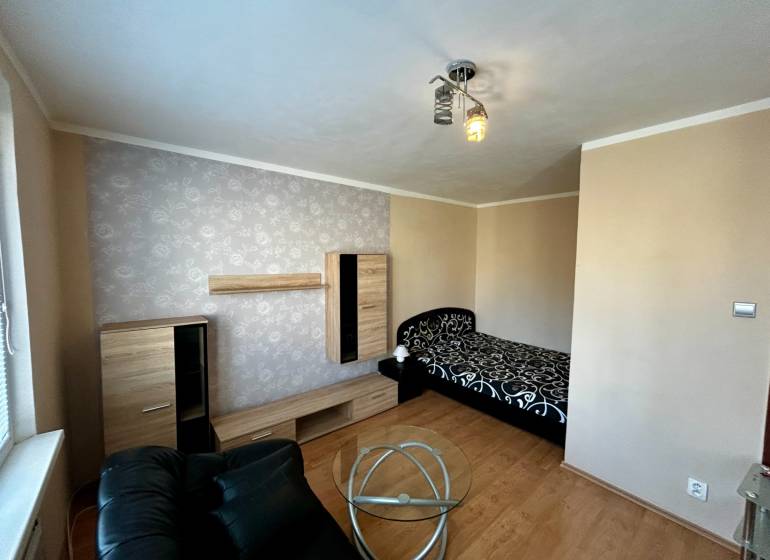 Ein Zimmer in einer Einzimmerwohnung mit einem Bett, einem schwarzen Sessel und einem Boden in Holzoptik.