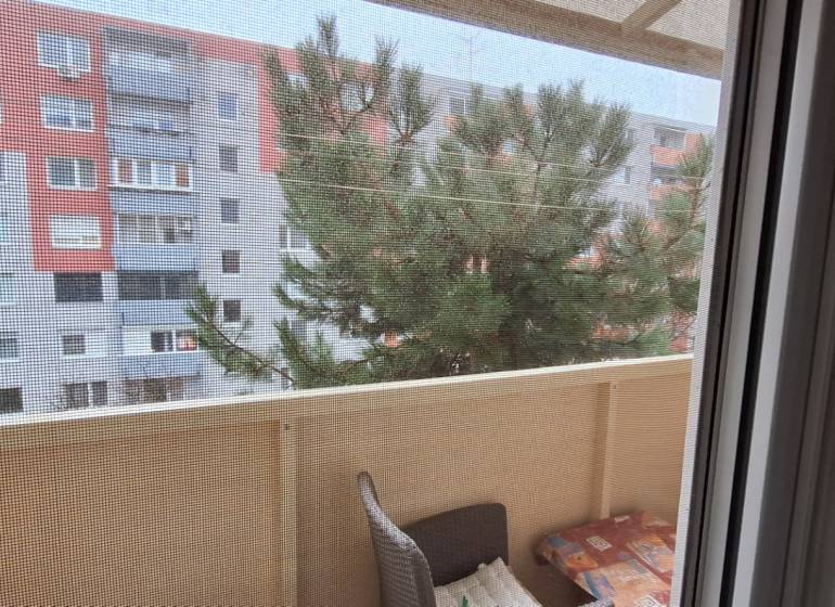 Der Balkon einer 2-Zimmer-Wohnung in Komárno mit Blick auf ein Plattenbau und einen Baum.