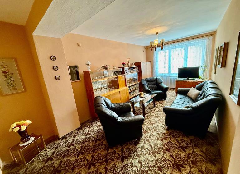 Wohnzimmer in einer Zweizimmerwohnung mit einer Couchgarnitur und einer verglasten Vitrine.