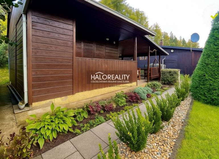 Eine Holzhütte in den Gärten in Bytča, umgeben von gepflegtem Grün und einem Weg aus Fliesen.