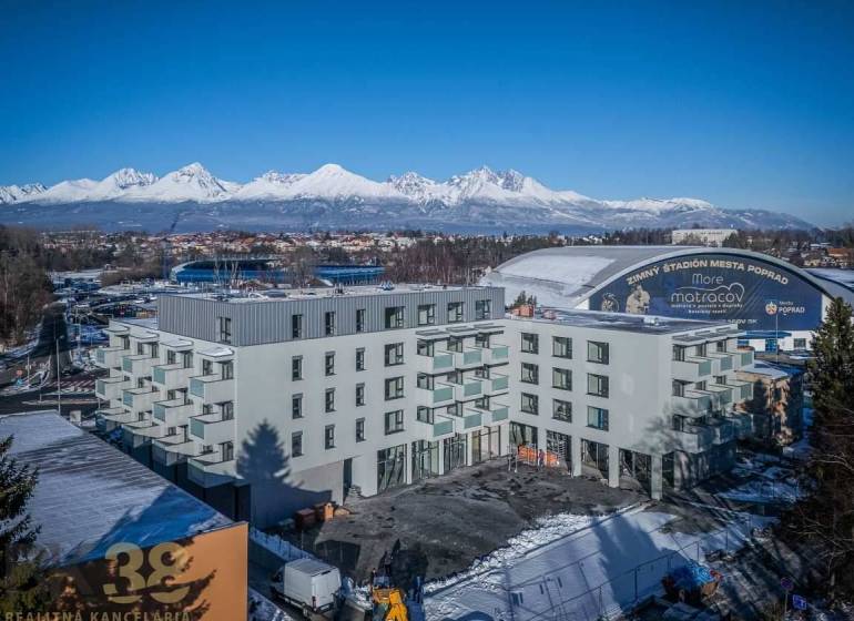 Ein Gebäude in Poprad mit den verschneiten Tatra-Bergen im Hintergrund und einem Winterstadion.