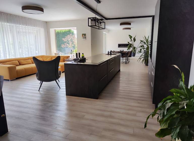 Küche und Wohnzimmer im Einfamilienhaus mit Insel, gelbem Sofa und Boden in Holzoptik.