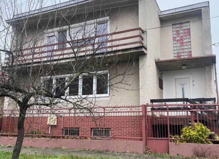 Ein Einfamilienhaus in Dlhá nad Váhom mit Betonfassade, Balkon und Vorgarten.