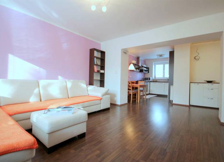 Wohnzimmer in einer 2-Zimmer-Wohnung mit einer Eckcouch und einem Boden in Holzoptik.