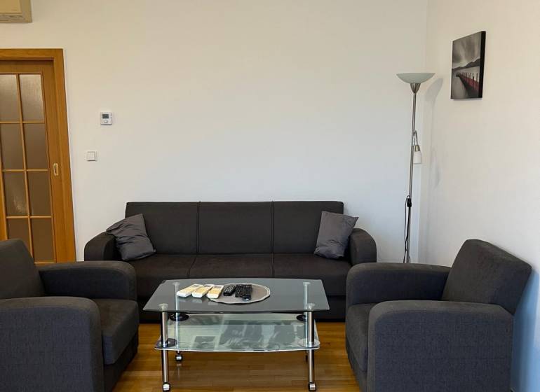 Graues Sofa in einer 3-Zimmer-Wohnung mit Holzboden und Glastisch.
