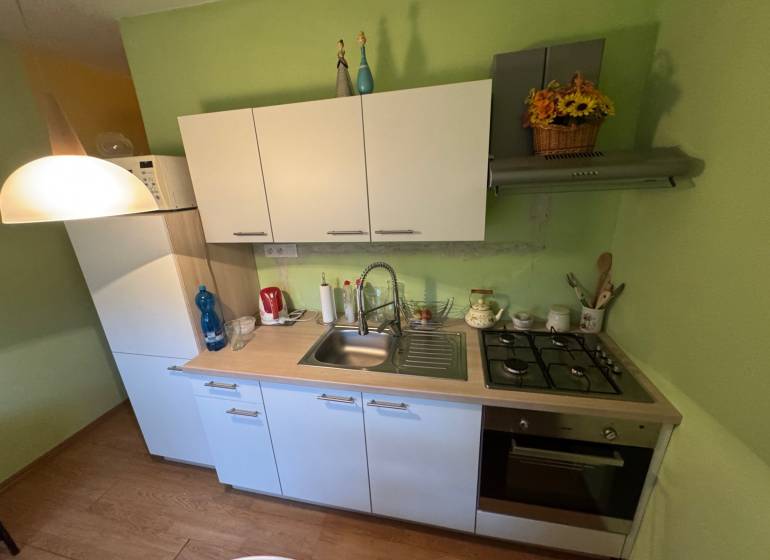 Küche in einer Einzimmerwohnung mit weißen Schränken und einem Boden in Holzoptik.