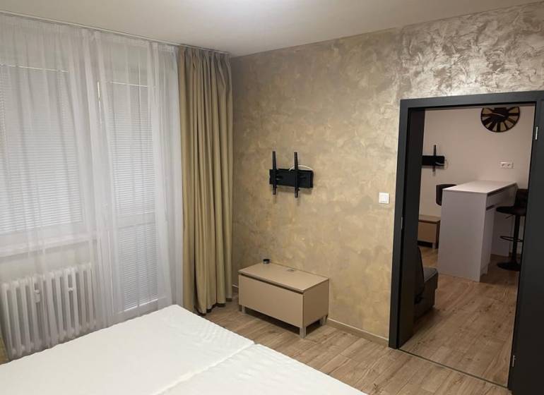 Innenraum einer Einzimmerwohnung mit Holzboden, Bett und Vorhängen am Fenster.