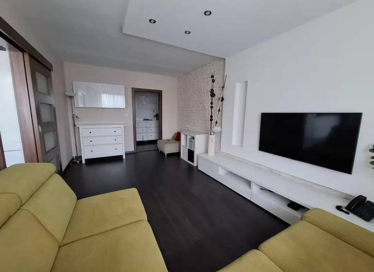 Wohnzimmer in einer 3-Zimmer-Wohnung mit Holzboden, Fernseher und Sitzgarnitur.