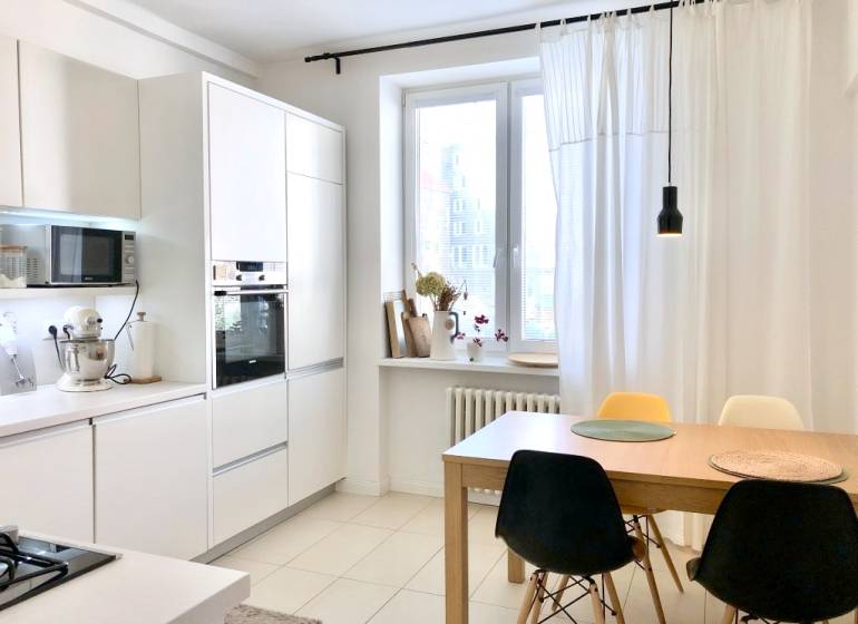 Küche in einer 2-Zimmer-Wohnung mit weißen Schränken und einem Esstisch mit Stühlen.