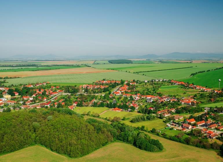 Luftaufnahme von Nemčiňany, umgeben von landwirtschaftlichen und forstwirtschaftlichen Flächen in einer grünen Landschaft.