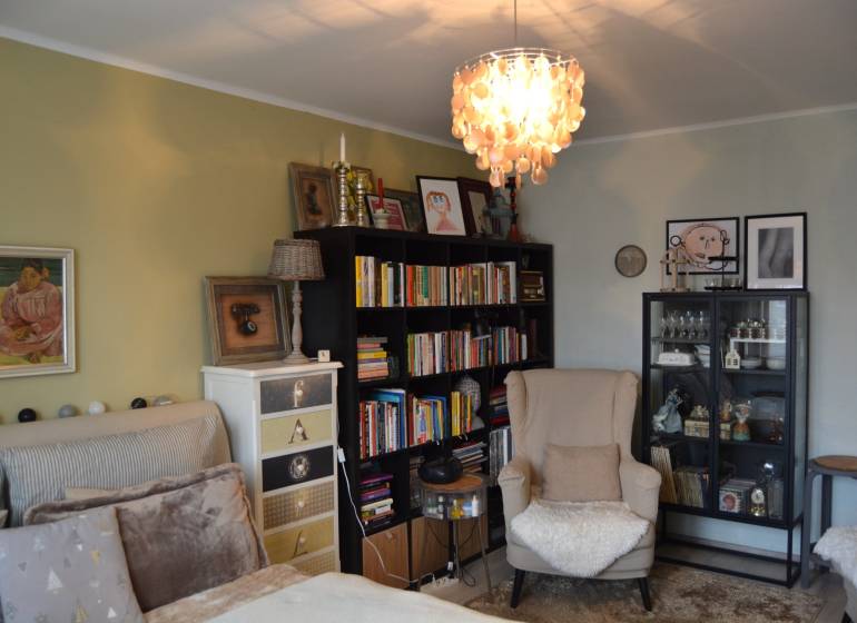 Ein Zimmer in einer 3-Zimmer-Wohnung mit einem Sessel, einem Bücherregal, Kronleuchtern und Dekorationen an den Wänden.