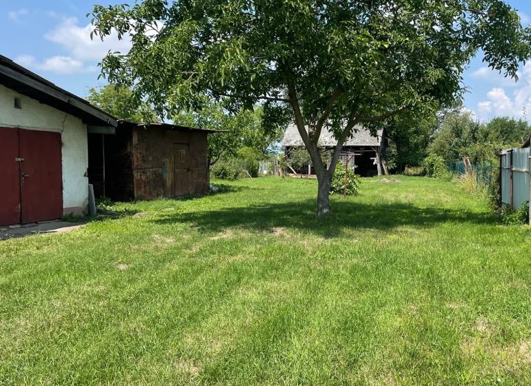 Ein Garten mit einem Holzbaum und einem Gebäude im Hintergrund in Zemplínska Široká. Grundstücke - Wohnen.