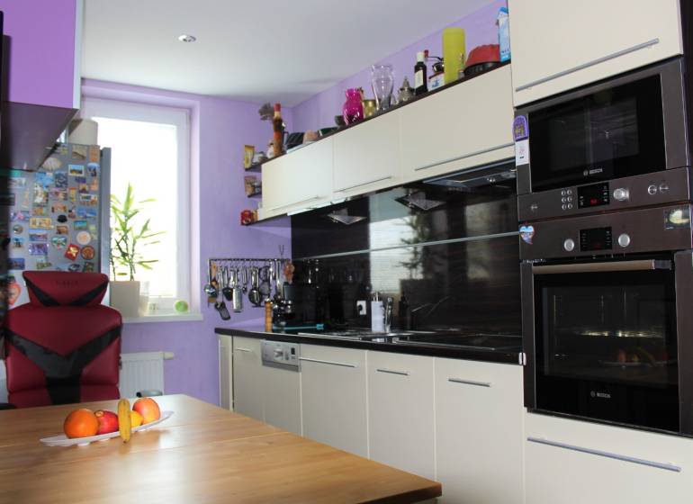 Küche in einer Einzimmerwohnung mit einem hellen Schrank, einem Stuhl und Obst auf dem Tisch.