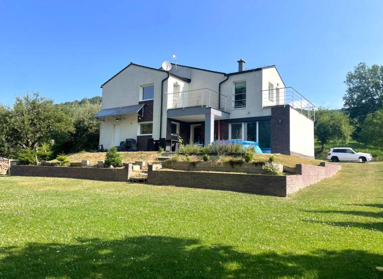 Ein Einfamilienhaus in Melčice-Lieskové mit gepflegtem Garten und Parkmöglichkeiten auf einem Rasenstück.