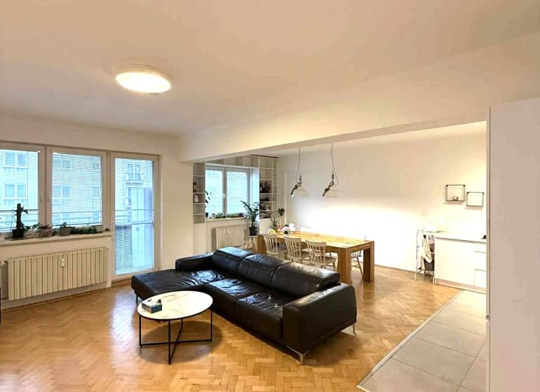 Wohnzimmer in einer 4-Zimmer-Wohnung mit Holzboden und schwarzem Sofa.