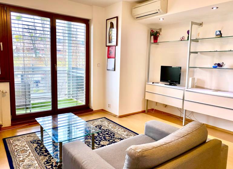 Wohnzimmer in einer 2-Zimmer-Wohnung mit Sessel, Glastisch und Boden in Holzoptik.