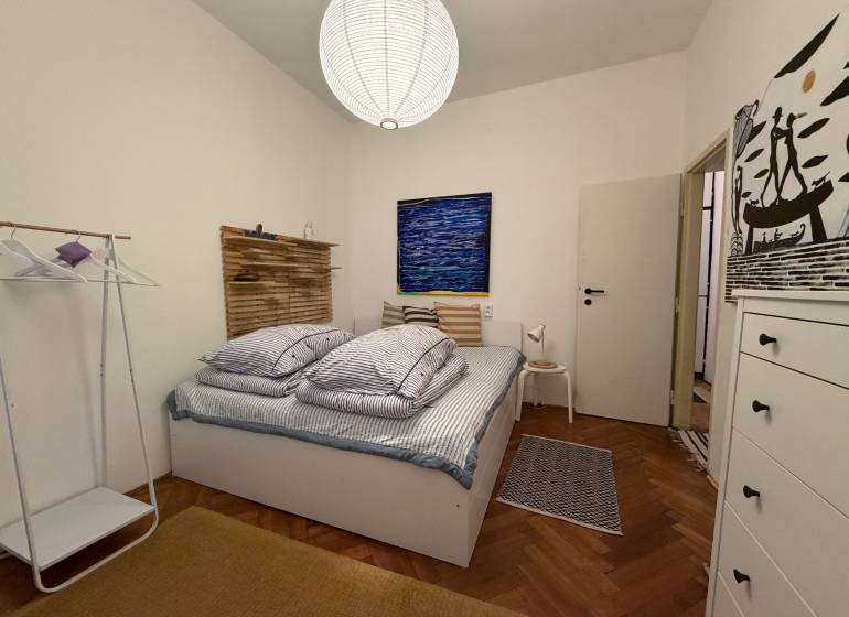 Schlafzimmer in einer 2-Zimmer-Wohnung mit Holzboden, Bett und weißem Schrank.