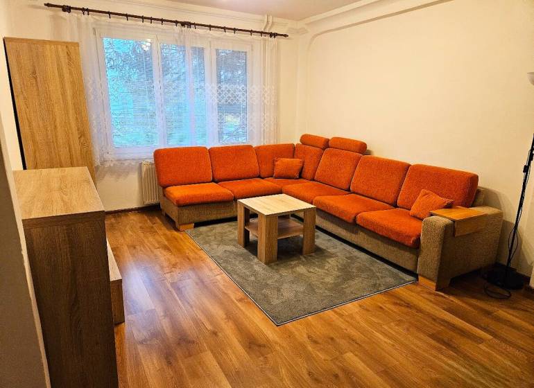 Wohnzimmer mit einem orangefarbenen Sofa und einem Boden in Holzoptik in einer 3-Zimmer-Wohnung.
