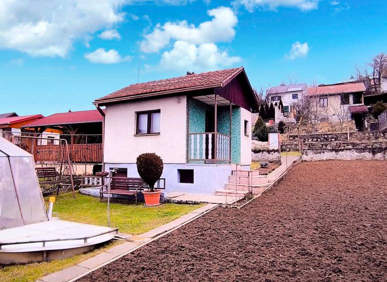 Ein Ferienhaus in Partizánske mit einem einfachen Garten, Bordsteinen und einem Pavillon unter blauem Himmel.