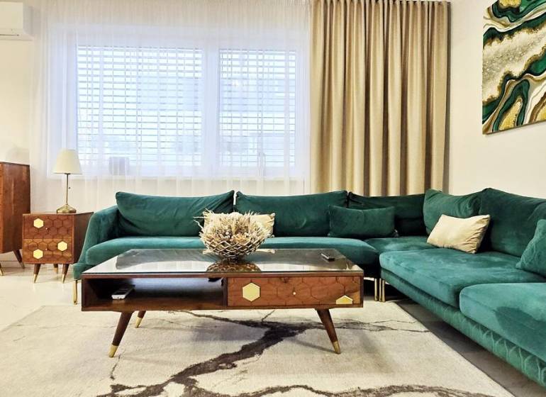 Ein Einfamilienhaus mit einem Sofa in Grüntönen, Holzmöbeln und Kunst an der Wand.