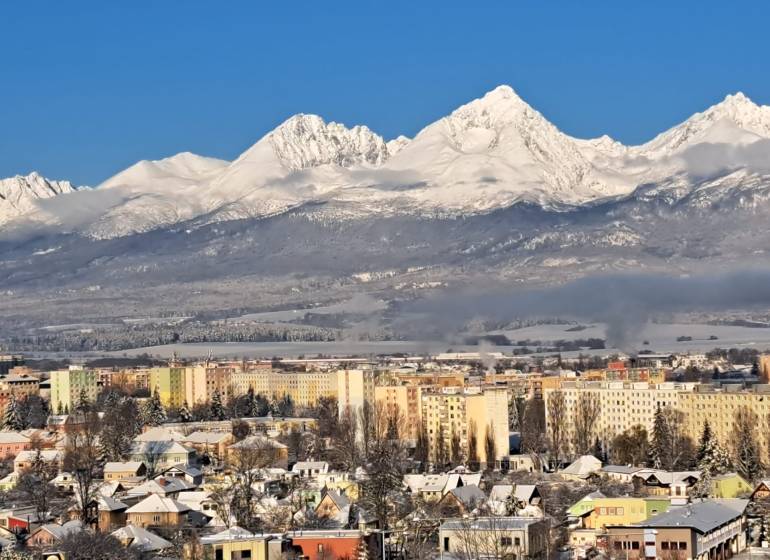 Verschneite Berge mit Blick auf einen Teil der Stadt Poprad und mehrstöckige Gebäude.