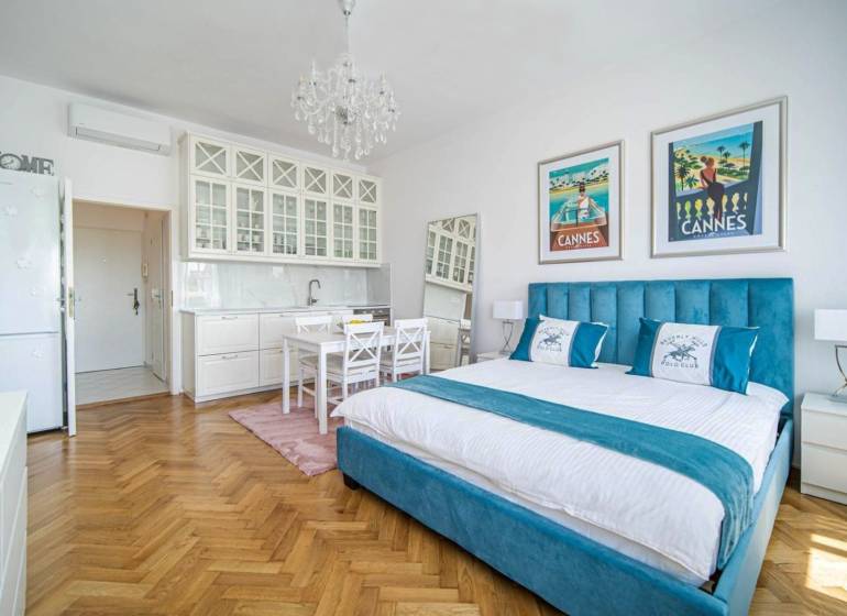 Einzimmerwohnung mit Holzboden, Bett und weißen Küchenschränken.